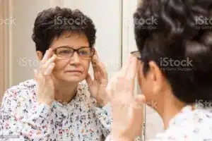 Senior woman trying on new eyeglasses and looking at herself in the mirror at home