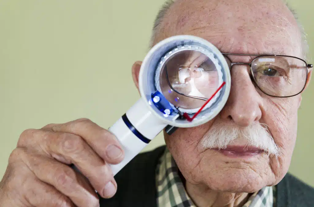 Older man holding a magnifying glass for an eye exam