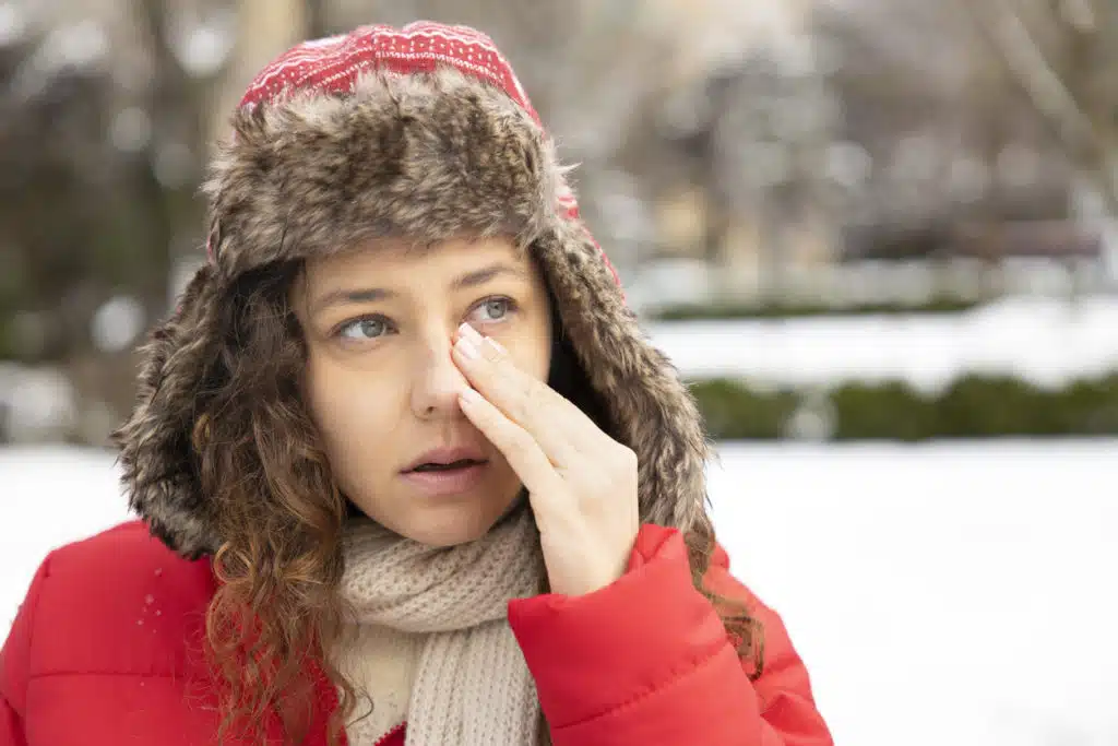 Young woman having itching eyes health problem. Sick woman in winter snow touching her sensitive eye
