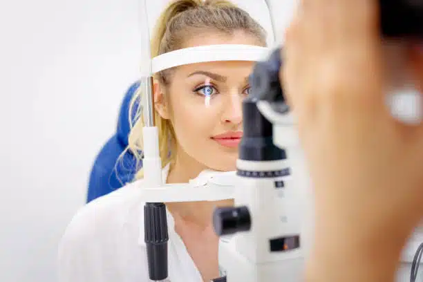 Beautiful young woman leaning her chin on ophthalmic refractor frame at the ophthalmologist's