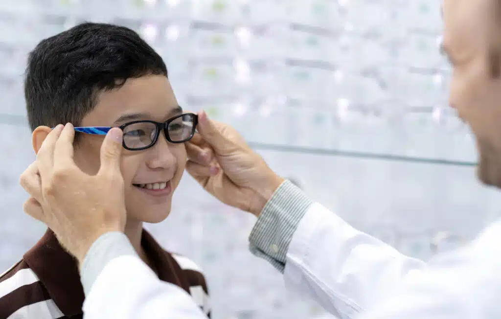 eye doctor puts new eyeglasses on the boy