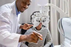 African young woman girl doing eye test checking examination with male man optometrist using phoropter in clinic