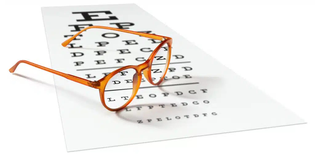 Orange eyeglasses sitting on visual test chart used for vision loss.