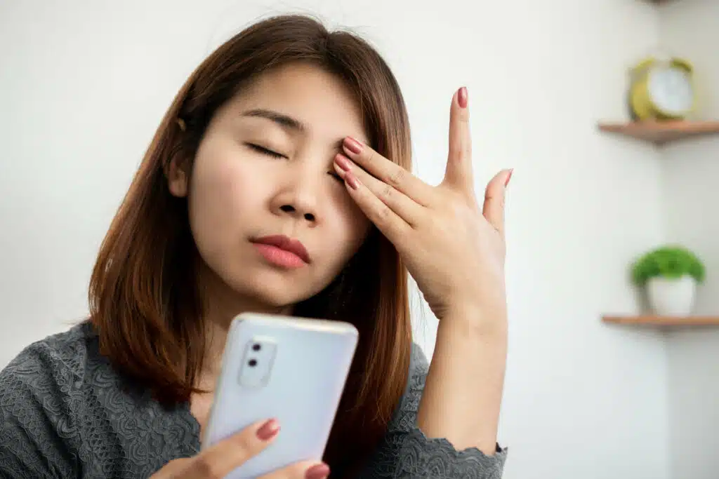 Asian woman suffering from eye pain from phone screen.